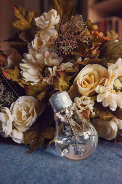 Lightbulb filled with water leaning against vintage flower bouquet, vertical