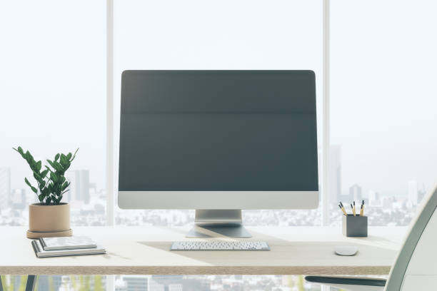 istock Front view on blank dark modern computer monitor on wooden table with flower pot, notebooks and keyboard in sunny office with city view from window. 3D rendering, mock up 1430388064