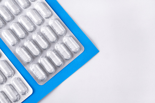 Capsule pills in blister pack on white and blue background. Medical and pharmaceutical backdrop. Mockup with copy space