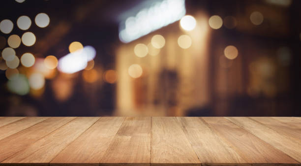 Selective focus.Wood table top with blur light bokeh in dark night cafe,restaurant background.