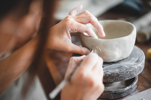 Selective focus. View of female hands works with clay makes future ceramic plate, ceramic artist makes classes of hand building in modern pottery workshop, creative people handcrafted design