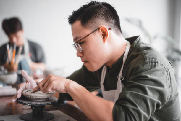 Happy Asian man working in pottery studio. Ceramic artist makes classes of hand building in modern pottery workshop, creative people handcrafted design stock photo