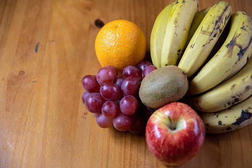 apple, banana, kiwi, grape and orange on a wooden table, top view with side space