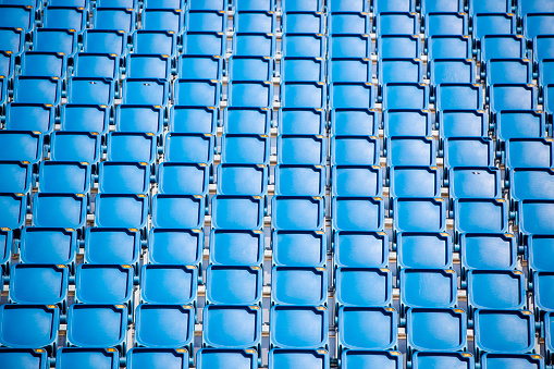 Empty blue and white seats in a footbal or soccer stadium. Grass field and plastic chairs, open door sports arena.
