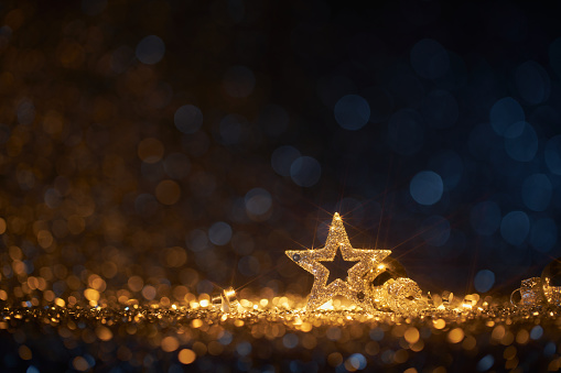 Still life photography of an abstract holiday / party  background. Shiny Christmas decoration on gold and blue defocused lights. Golden shiny glitter, lens flares, and defocused blue lights. Native image size: 7952x5304