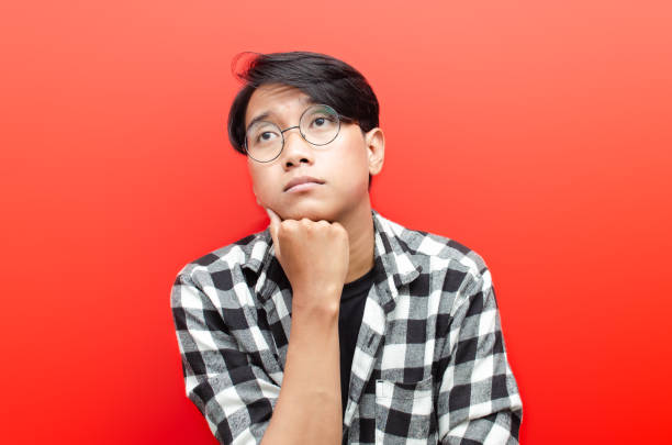 young asian man looks clueless, puzzled, confused, stressed and wondered with hand gesture asking why. isolated over red background. billboard advertisment model concept. - blank expression head and shoulders horizontal studio shot imagens e fotografias de stock