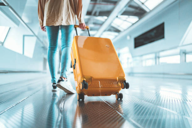 Female traveler walking with a yellow suitcase at the modern Airport Terminal, Back view of woman on her way to flight boarding gate, Ready for travel or vacation journey stock photo