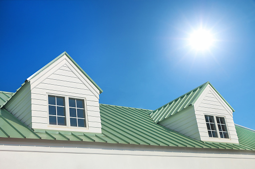 dormer with windows on metal sheet roof with blue sky and sunshine.