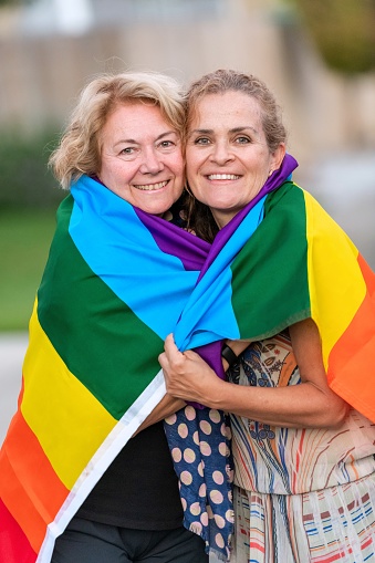 Smiling happy Mature lesbian couple posing wrapped in a rainbow flag