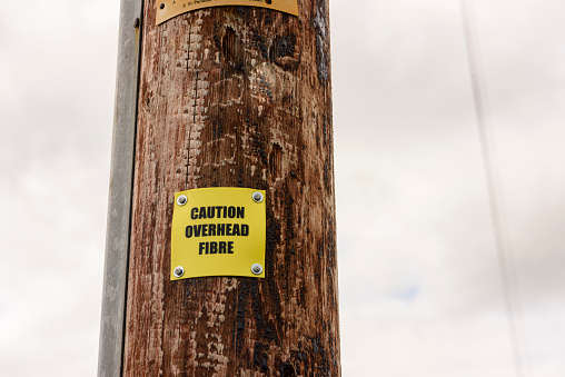 Sign on a wooden telephone pole warning people that the pole is carrying fibre optic cable.