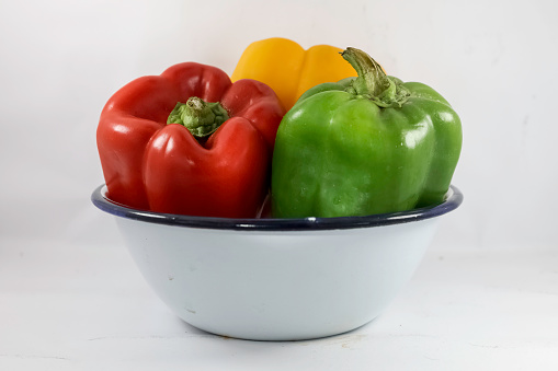 Green, red, yellow bell peppers in white ceramic bowl