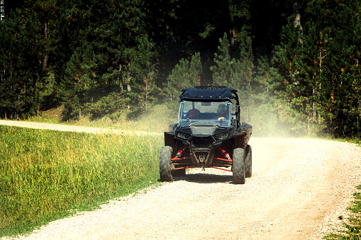 One black off-road side by side vehicle on mountain dirt and gravel road with one person driving and dust boiling up behind the vehicle.