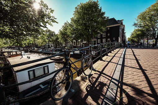 Morning View Of Tree Shadows And Bicycle Parked On Canal Bridge In Amsterdam, The Netherlands