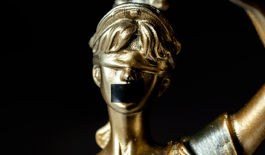 Lady Justice with black tape over his mouth.