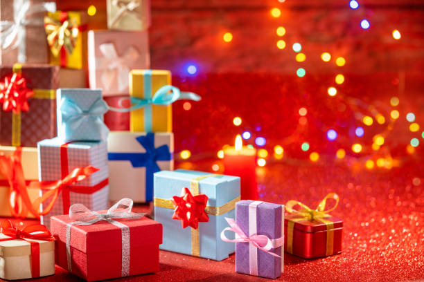 Many gift box stacked as a Christmas gift boxes arrangement on red glitter background with christmas lights