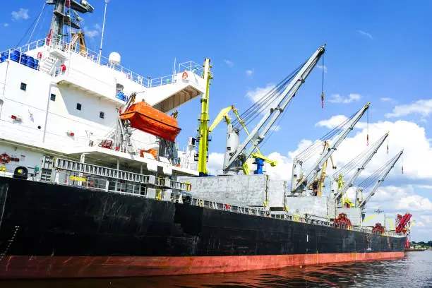 Photo of Large bulk cargo ship with open holds in the port cargo terminal, blue sky background