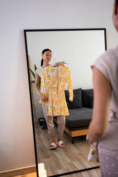 istock A young Asian woman looking at her reflection in a mirror while choosing a dress 1430447966