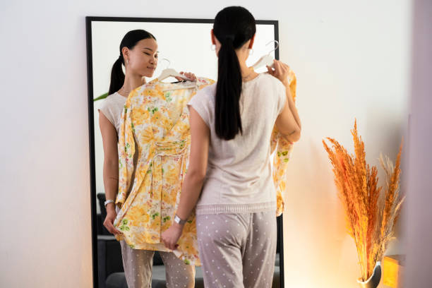istock A young Asian woman looking at her reflection in a mirror while choosing a dress 1430448063
