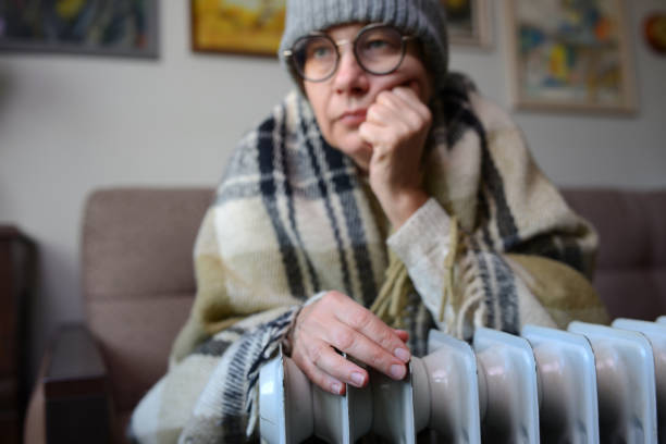 la mano di una donna viene riscaldata su una stufa elettrica. una donna sta congelando a casa, seduta vicino al radiatore in un cappello caldo e una coperta. - pelle d'oca foto e immagini stock