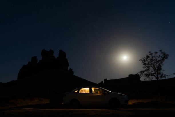 parked car in the countryside at dusk. The interior lights of the vehicle visible in the moonlight are on. fairy chimney and tree silhouette appear. Shot with a full frame camera.
