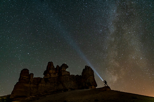man climbing fairy chimneys in milky way landscape. The moonlight is long exposed to create a burst of light effect. lonely man under the stars. Shot with a full frame camera.
