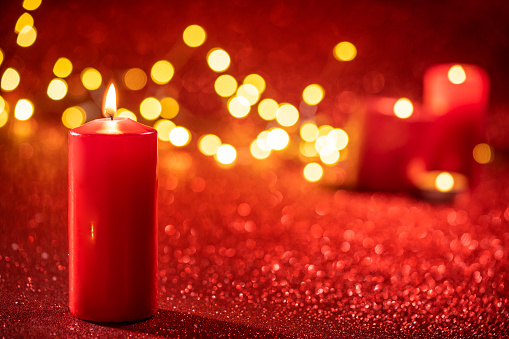 Red candle light Christmas candlelight on glowing flame sparkling red background blurred