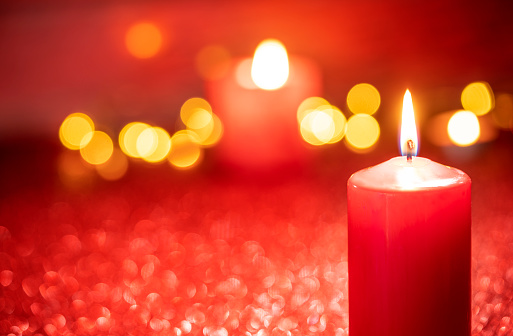 Red candle light Christmas candlelight on glowing flame sparkling red background blurred