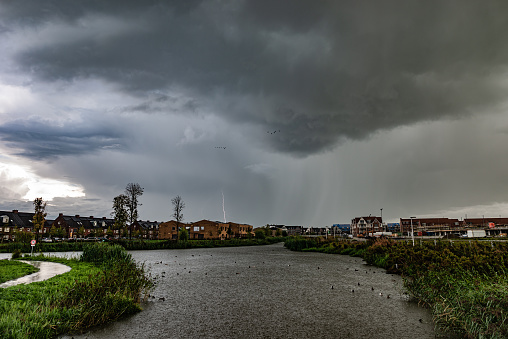 Dramatic clouds and lightning strike during a thunderstorm with heavy rain falling in the water of a pond.