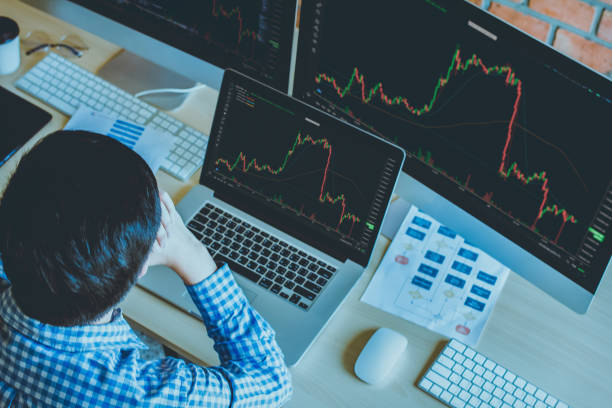 istock businessman 30s looking at stock tickers or graphs cryptocurrency trading platforms on a laptop with a cup of coffee, paperwork on the table at home office in the morning. Top view Selective focus 1430471253