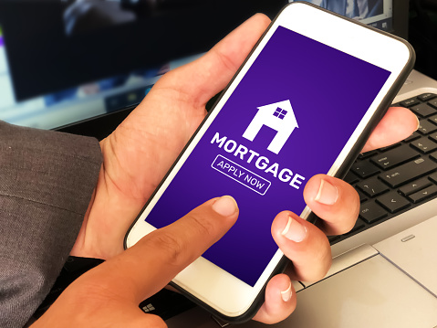 Applying for a mortgage through smartphone concept Backdrop with laptop in the background. Modern mortgage process