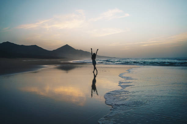 giovane donna che si gode il tramonto sulla spiaggia vuota - light sea low tide fuerteventura foto e immagini stock