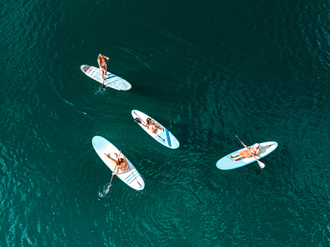 Group of four unrecognizable women paddle boarding on a lake, top down aerial view, deep dark blue lake water and paddle boards.