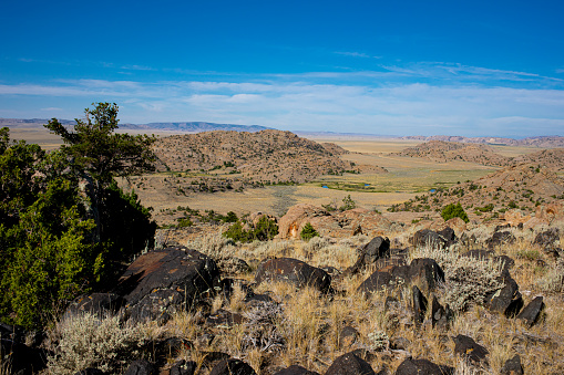 Black boulders of amphibolitic dike surrounded by granitic boulders overlooking Sweetwater River valley in the Granite Mountains of Wyoming with blue sky and sparse cirrus clouds