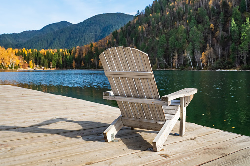 white Adirondack chair on a wooden dock overlooking a calm lake. beautiful landscape of mountain lake, vacation in the mountains, luxury autumn vacation concept