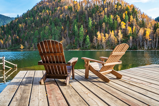 Two Adirondack chairs on a wooden dock overlooking a calm lake.