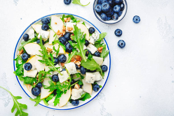 istock Delicious arugula salad with pears, blueberries, roquefort cheese and walnuts. Black kitchen table background, top view 1430508303