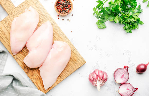 Raw chicken breast fillet, meat on cutting board prepared for cooking with garlic, thyme, spices and pepper. White kitchen table, top view Raw chicken breast fillet, meat on cutting board prepared for cooking with garlic, thyme, spices and pepper. White kitchen table, top view CHICKEN BREAST stock pictures, royalty-free photos & images