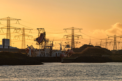 Rotterdam, Netherlands - November 22 2021 : a highly polluting black coal power plant and power lines coming out of it at sunset while rescue boat is hanging on a crane