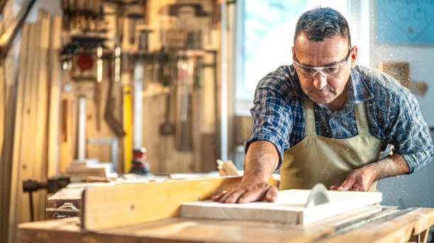 Mature professional worker concentrated on work Sawing material on circular saw. Mature professional worker concentrated on work. Wood material processing in carpentry, handmade craftwork products. carpentry stock pictures, royalty-free photos & images
