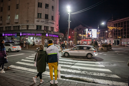 Picture of people waiting for green light to cross a crossroad in the city center of Belgrade, at night, during heavy rains, in autumn.