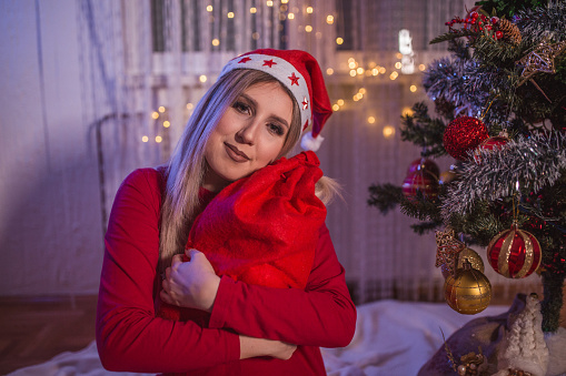 A beautiful, young, blonde woman decorates a Christmas tree in her house. New Year's euphoria!