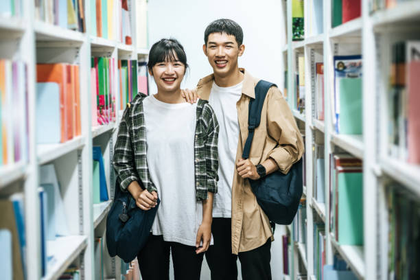 Men and women carrying a backpack and searching for books in the library. stock photo