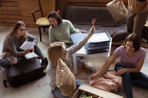 istock Playful talking active, friendly women sit on floor, taking scissors for unpacking luggage in room. Check list of things 1430535399