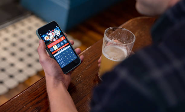 Man gambling online while drinking beer at the pub Close-up on a man gambling online using a mobile app on his cell phone while drinking beer at the pub sports betting stock pictures, royalty-free photos & images