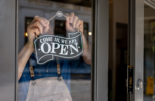 Primer plano del dueño de un negocio colgando un letrero abierto en la puerta de su restaurante photo