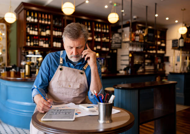 Restaurant owner talking on the phone while working on the accountancy Business owner talking on the phone while working on the accountancy at a restaurant - Small business concepts ipad calculator stock pictures, royalty-free photos & images