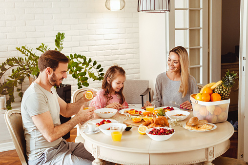 Cheerful happy family sitting at the table, having healthy breakfast in the morning, still waring pyjamas