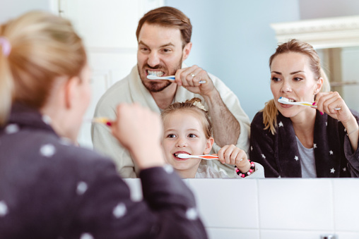 Smiling happy family in front of a mirror, brushing their teeth