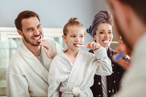 Smiling happy family in front of a mirror, brushing their teeth