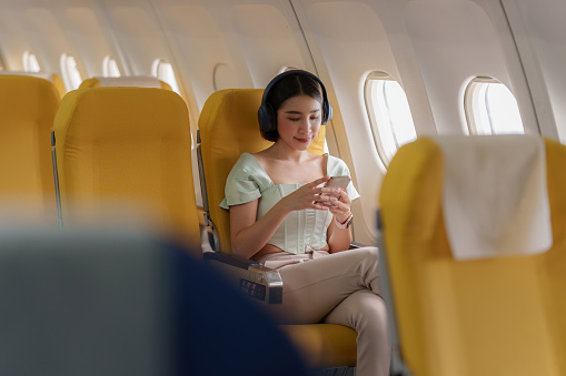 Young asian woman using smartphone connected to wifi internet during flight on board. Travel concept.